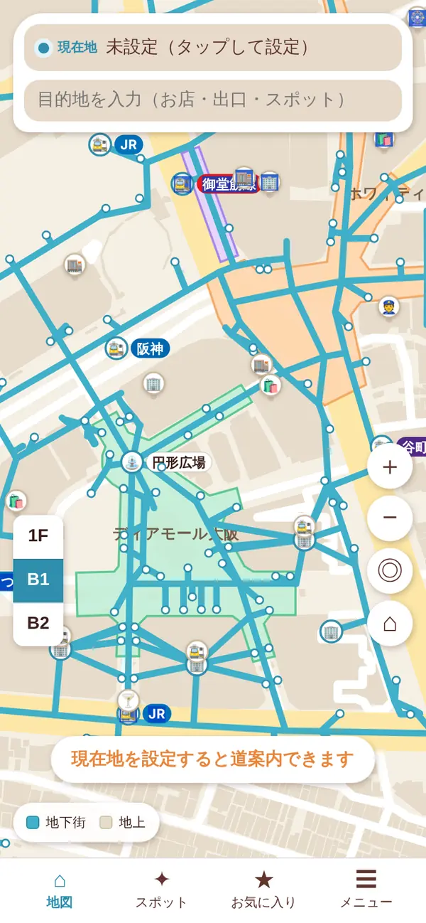北が上の平面の地図。ベージュの地上の道路と建物の上に、地下街の床が地下街ごとの色（緑・橙など）で塗られ、通路が青い線で描かれている。改札や建物はアイコンで出ている